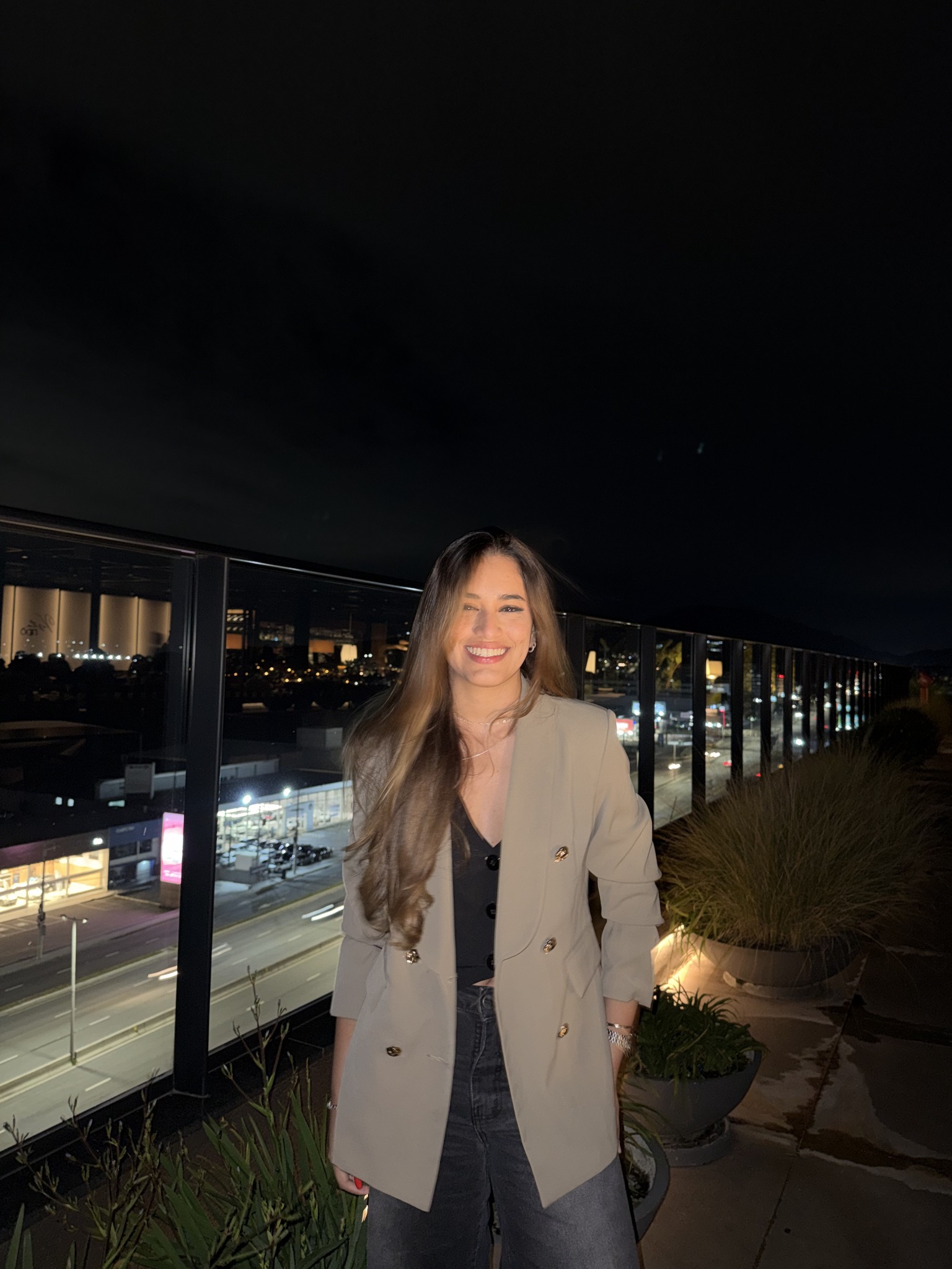 Isis Santos, fundadora e diretora criativa da ONZE, sorrindo em um terraço à noite, com a cidade iluminada ao fundo.